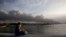 Una mujer contempla desde el malecón el humo del incendio en la Base de Supertanqueros de crudo en la Bahía de Matanzas, este martes, 9 de agosto. (AP Foto/Ismael Francisco)