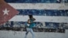 Una mujer camina en la calle. Detrás de ella hay una pared con la bandera de Cuba pintada. (YAMIL LAGE / AFP)