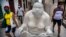Transeúntes pasan junto a una de las estatuas de Xu Hongfei en La Habana, a la que alguien añadió un nasobuco. (AP/Ramon Espinosa)